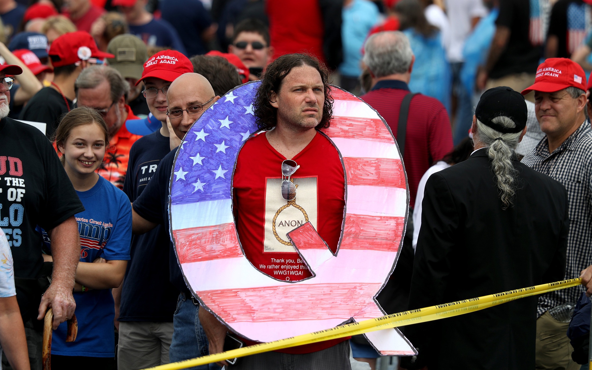 Image:  David Reinert holds a large "Q" sign while waiting to see Trump