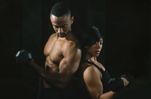 Young African American Couple Lifting Weights Together In Gym