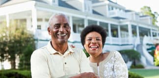 Mature African American couple (50s and 60s) at a country club, standing in front of clubhouse. Main focus on woman.