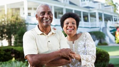 Mature African American couple (50s and 60s) at a country club, standing in front of clubhouse. Main focus on woman.