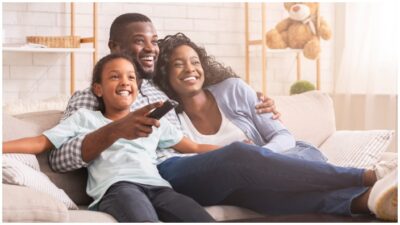 Happy African American family relaxing and watching tv at home, enjoying weekend together.