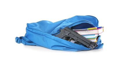 Gun in backpack with books - Depositphotos