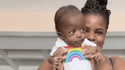 Mother holds up newborn baby wearing rainbow onesie