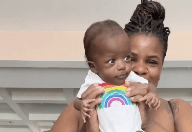 Mother holds up newborn baby wearing rainbow onesie