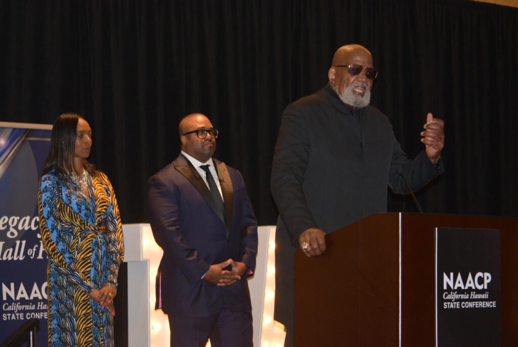 Dr. Harry Edwards (Legacy Hall of Fame recipient), at the podium, and Dr. Kenneth Noel organized the protest at the 1968 Olympics in Mexico City. He is shown here with CA/HI NAACP President Rick Callendar and Carolyn Veal-Hunter (CA/HI NAACP treasurer) at the Legacy Hall of Fame induction ceremony in Sacramento. June 24, 2023. CBM photo by Antonio Ray Harvey.