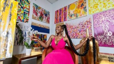 Dunnie O wearing a pink dress, sitting in front of canvas paintings that she made