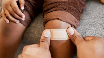 Parent childcare, knee injury and plaster on child leg after getting hurt showing care, love and support to help growth and childhood development. Hands closeup of adult applying bandage to kid stock photo
