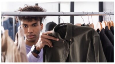 Young african american owner of showroom working with clothes on hangers on blurred foreground
