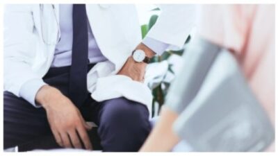 doctor sitting in front of patient with blood pressure gauge on hand