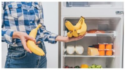 Cropped view of woman holding bananas near open fridge