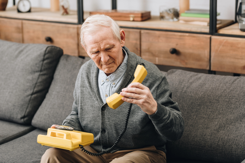 Retired man looking at old phone while sitting on sofa