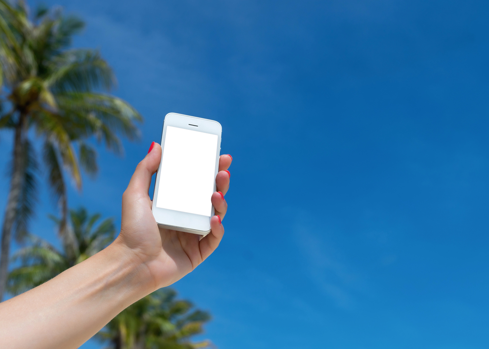 Woman hand showing a blank smart phone on the beach
