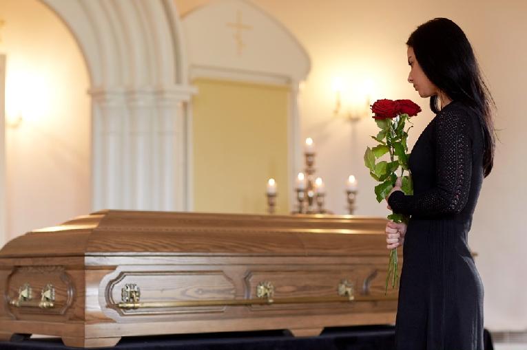 Virginia Funeral Home Sued After Maggots Found in Body // Woman with red roses and coffin at funeral - Depositphotos