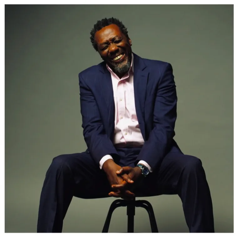 Actor Edwin Lee Gibson, star of FX&rsquo;s THE BEAR, wearing a navy suit and pink shirt, smiling and laughing during a studio photoshoot.