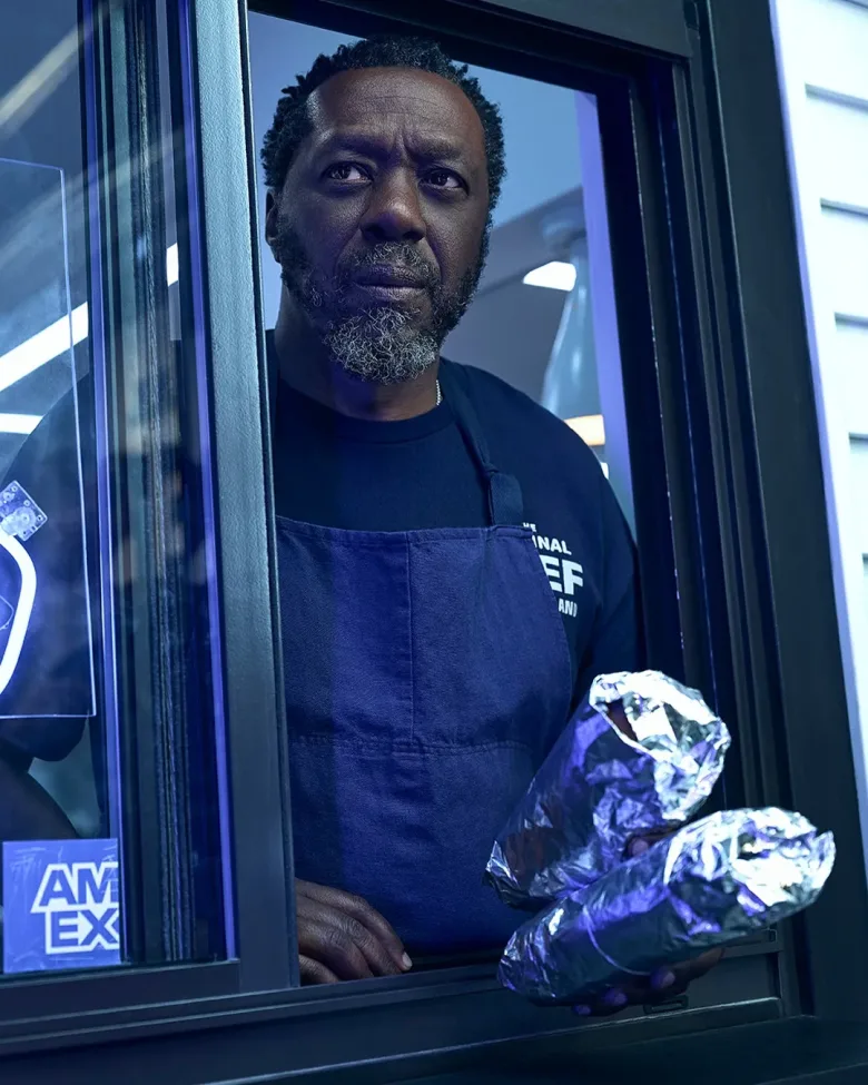 Edwin Lee Gibson as Ebraheim in FX&rsquo;s &ldquo;The Bear,&rdquo; wearing a dark apron and standing at a drive-thru window holding wrapped sandwiches.