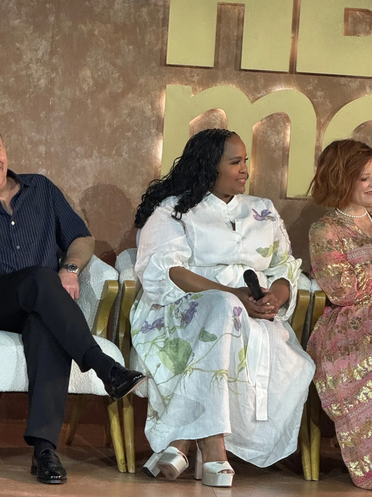 Natasha Rothwell seated center during an HBO Max Emmy panel, wearing a white floral dress and holding a microphone, flanked by other panelists.