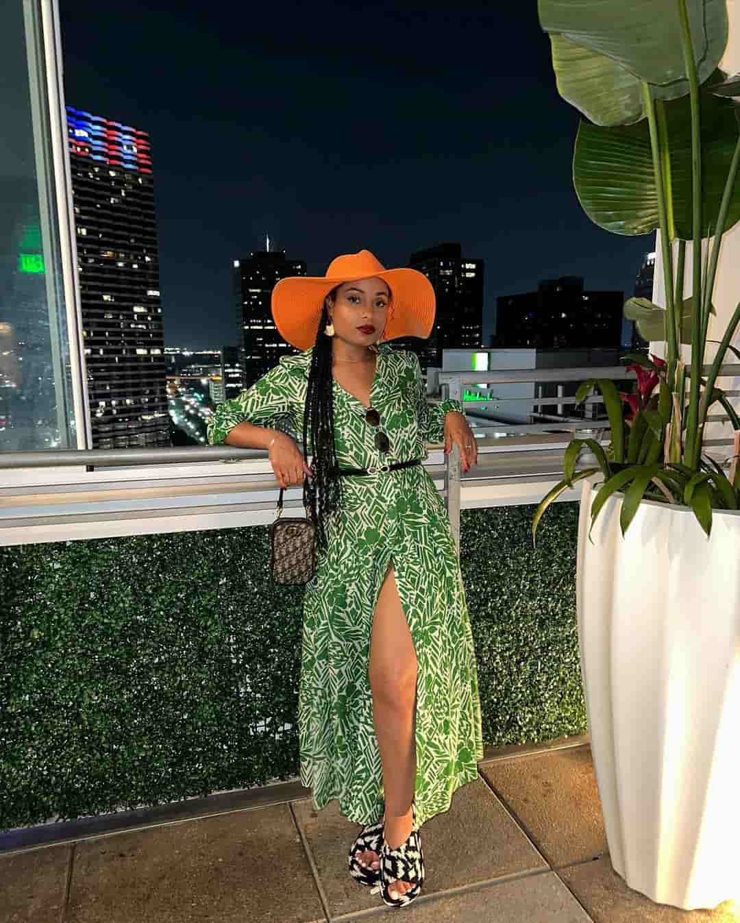 Hannaha Hall posing on a rooftop at night in a patterned green dress and wide-brimmed orange hat