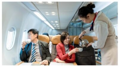 Flight attendant pouring hot coffee for female business passenger during inflight meal service on airplane, demonstrating excellent airline hospitality stock photo