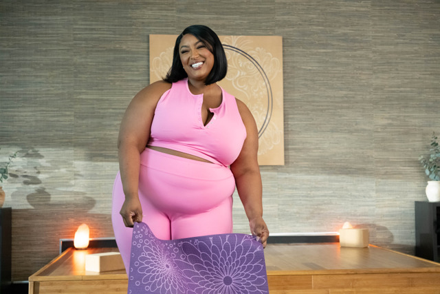 Nzinga Imani smiles while holding a yoga mat in a still from &ldquo;Zatima.&rdquo;