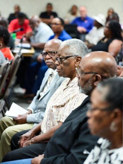 A community town hall scene showing elderly Black renters confronting representatives over rising rents / via GrokAI