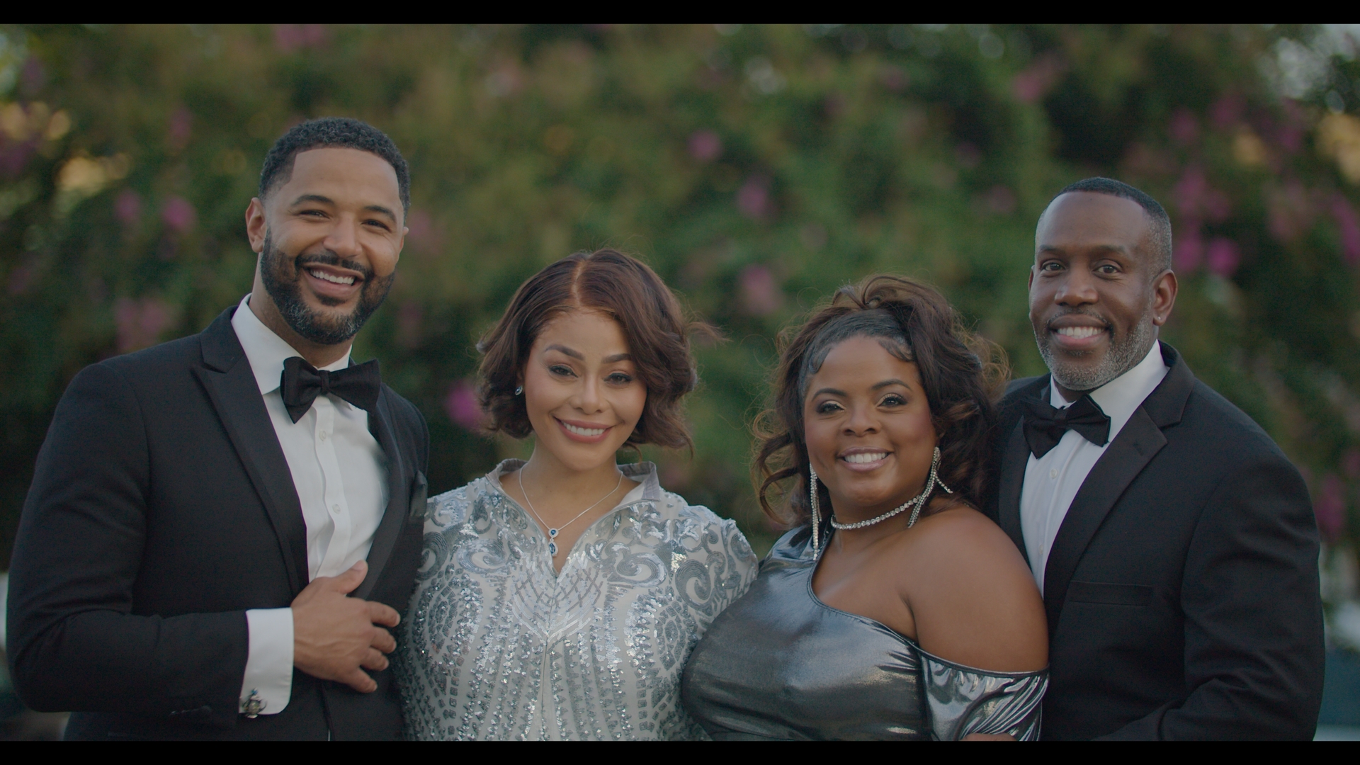 Brely Evans standing second from right in a formal outdoor group photo with cast members dressed in evening attire.