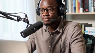 A Black journalist working independently from home, surrounded by podcast gear, a laptop, and cultural books, representing self-reliance - via GrokAI