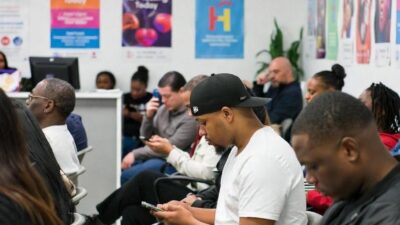 A diverse group of people waiting at a community health clinic in New York City, with posters about HIV awareness on the walls - via GrokAI