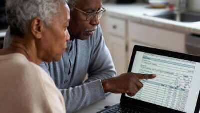 A senior couple checking their finances at a kitchen table with a laptop open, showing a Social Security payment calendar for 2026 - via GrokAI