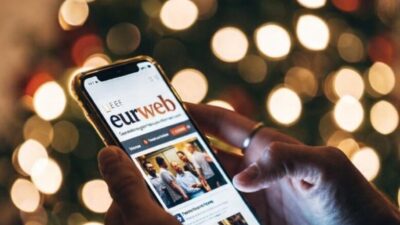 Someone holding a smartphone while reading news on EURweb at night - blurred Christmas lights in the background - via eurAI
