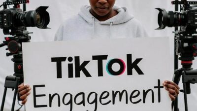 A content creator holding a sign that says 'TikTok Engagement Down' while packing up filming gear, suggesting burnout or frustration post-sale - via eurAI