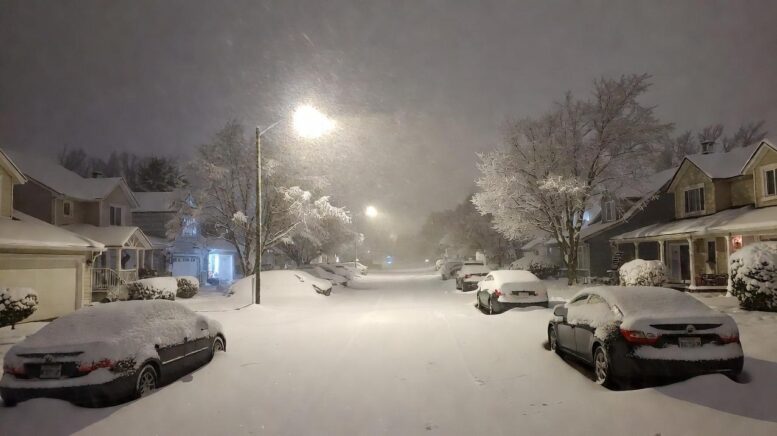 A snow-covered suburban street with cars half-buried, streetlights glowing through heavy snowfall - via eurAI