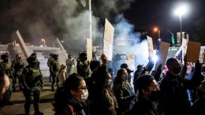 A tense nighttime protest scene in Minneapolis with tear gas in the air - via eurAI