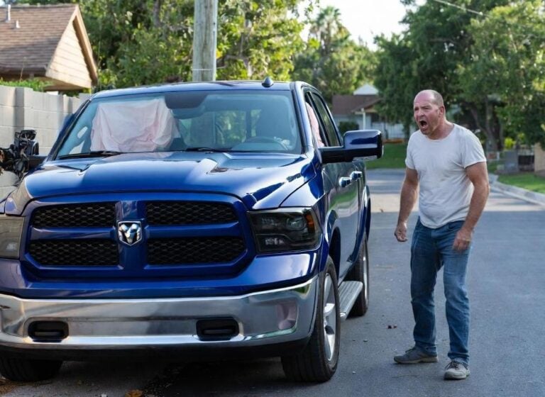 Angry white man standing next to his crashed pick-up truck - via eurAI