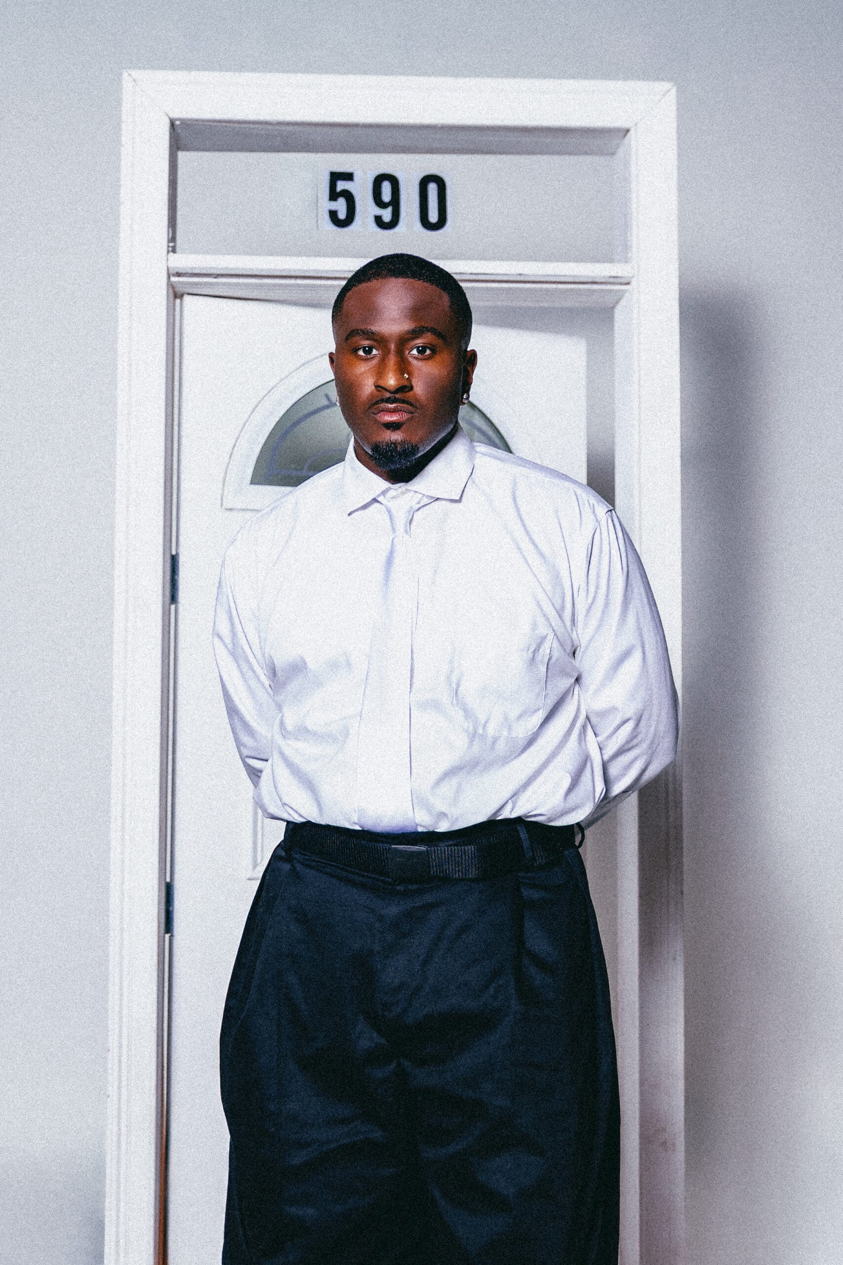 Ben Reilly standing in a white button-up shirt in front of a door marked 590