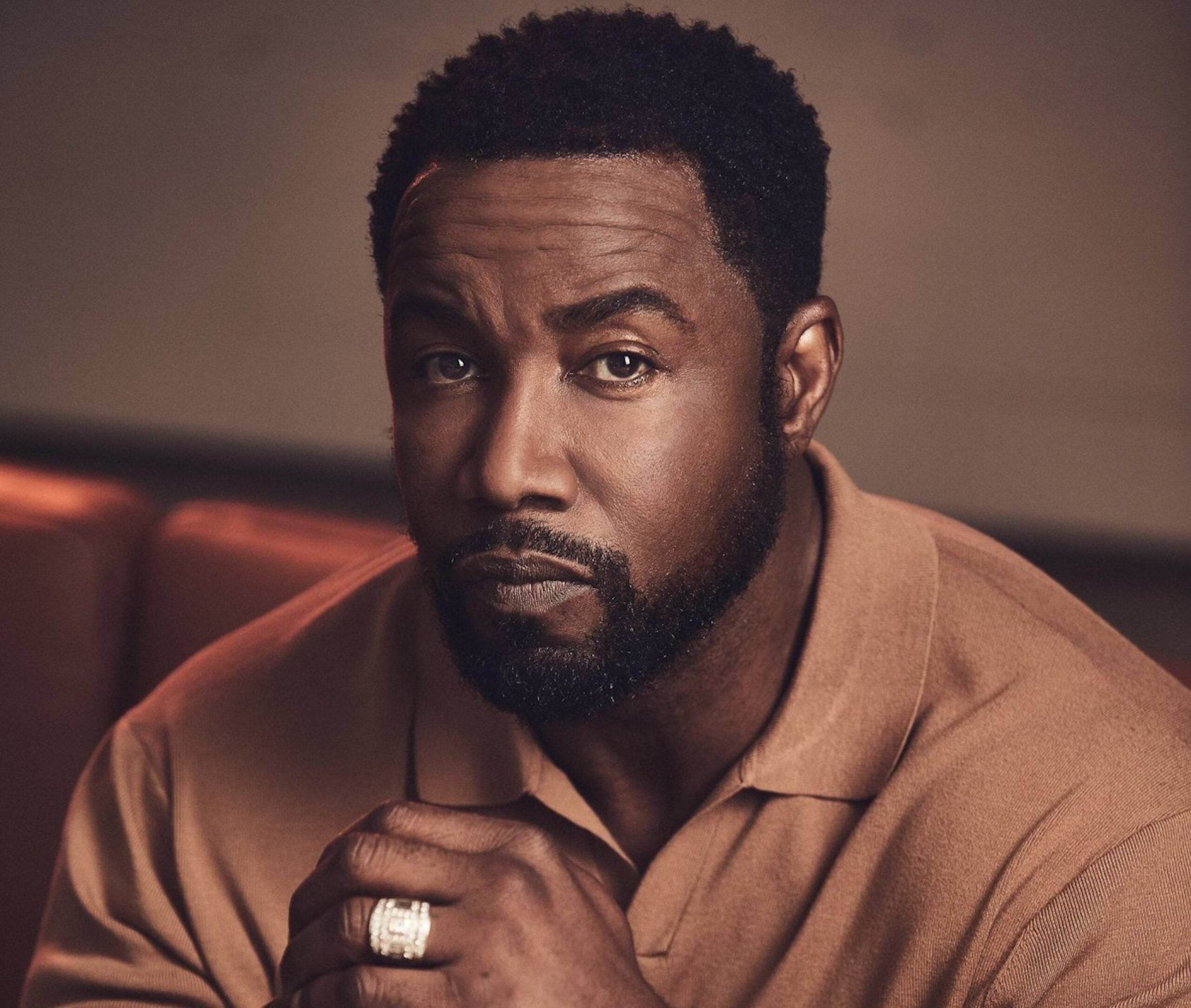 Michael Jai White poses in a close-up portrait wearing a tan shirt with his hand resting under his chin