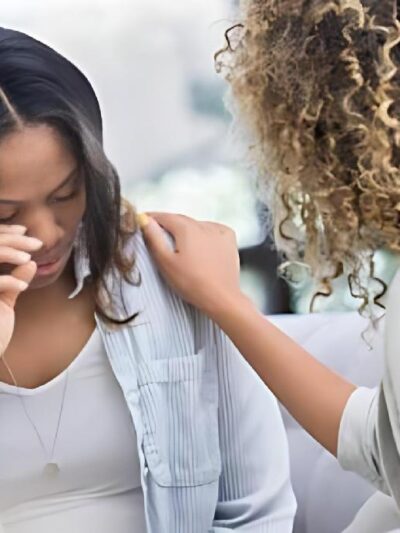 Caring therapist places her hand on a young woman's shoulder as the woman cries during a therapy session