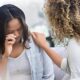 Caring therapist places her hand on a young woman's shoulder as the woman cries during a therapy session