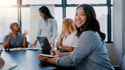 Business meeting, portrait and woman writing with team for planning, strategy and marketing idea in office. Design, collaboration and face of designer with notes for group project, vision and mission