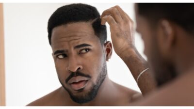 Close up anxious unhappy African American man checking hair after shower, looking in mirror, standing in bathroom at home, dissatisfied by hair loss or dandruff, healthcare and beauty concept