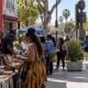 Black vendors and residents at a busy Los Angeles (Leimert Park) outdoor marketplace with runners visible in the background - via eurAI