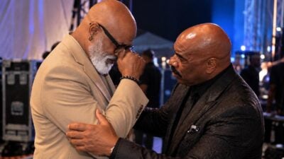 Editorial depiction of two Black comedians (Jonathan Slocumb and Steve Harvey) reconciling backstage