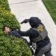 A screenshot from video shows a federal agent shoving a bystander into hedges and aiming a gun as a pedestrian&rsquo;s dog barks at the confrontation