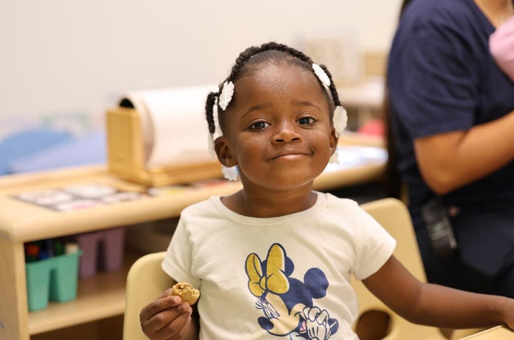 Smiling young girl enjoys a snack at preschool